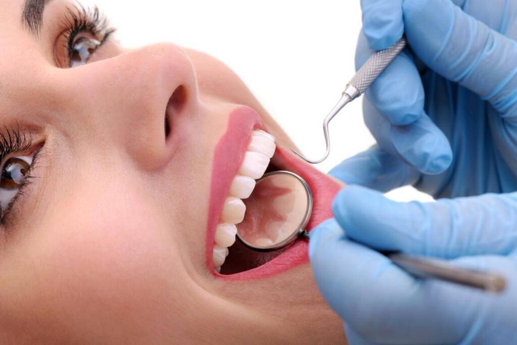 Frau mit schwarzem Haar wird beim Zahnarzt behandelt. Eine Hand mit blauen Handschuhen arbeitet in ihrem Mund, Prophylaxe